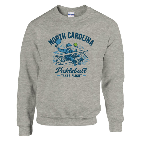 Pickleball sweatshirt featuring Orville Wright's first flight holding a pickleball with the text “North Carolina Pickleball Takes Flight”.