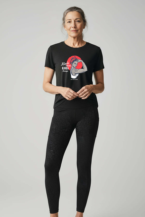 Confident woman in her 70s wearing black leopard constantly varied gear leggingsin and Kinda Vintage Kinda Savage Rosie unisex triblend t-shirt in black.