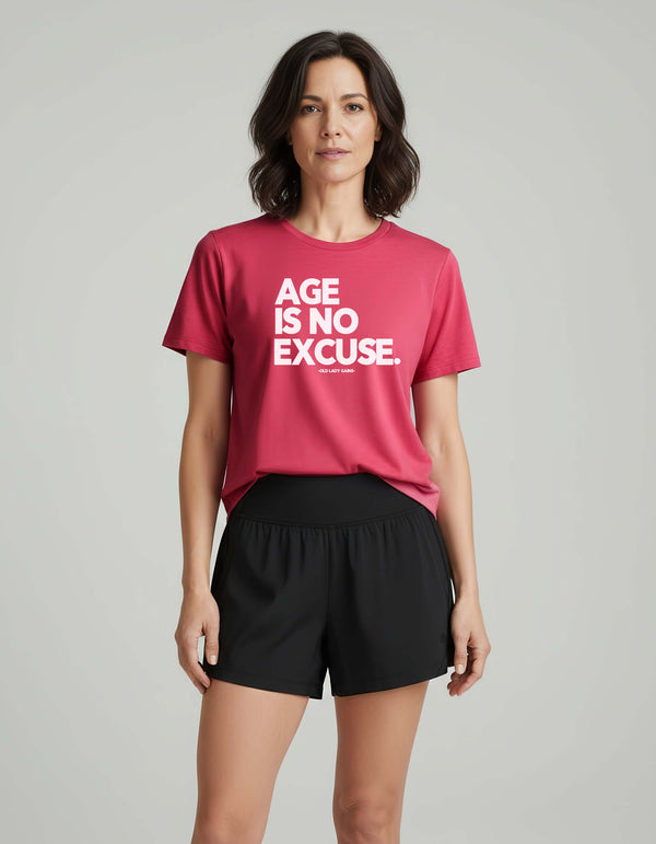 strong Woman over 40 wearing a berry t-shirt with 'AGE IS NO EXCUSE' text on a gray background