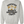 A light heather gray crewneck sweatshirt featuring a vintage-style graphic on the front with a cartoon illustration of an older woman lifting a barbell and the text 'CERTIFIED HEAVY EQUIPMENT Operator'.