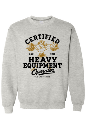 A light heather gray crewneck sweatshirt featuring a vintage-style graphic on the front with a cartoon illustration of an older woman lifting a barbell and the text 'CERTIFIED HEAVY EQUIPMENT Operator'.