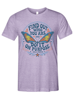 A heather purple short-sleeve t-shirt with a colorful graphic on the front featuring a butterfly and the text 'FIND OUT WHO YOU ARE AND DO IT ON PURPOSE' by Dolly Parton.