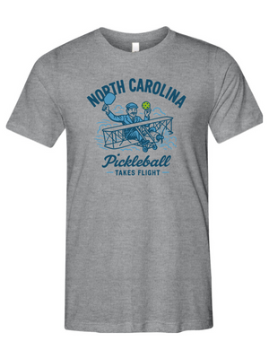Gray t-shirt with blue graphic and text 'North Carolina Pickleball Takes Flight' on a white background
