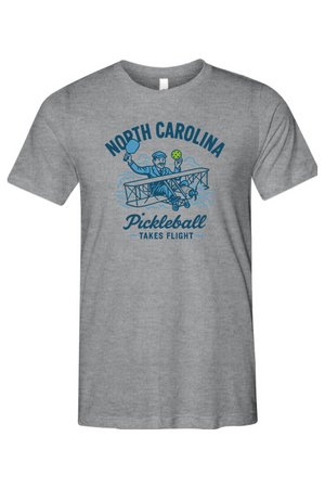 Gray t-shirt with blue graphic and text 'North Carolina Pickleball Takes Flight' on a white background