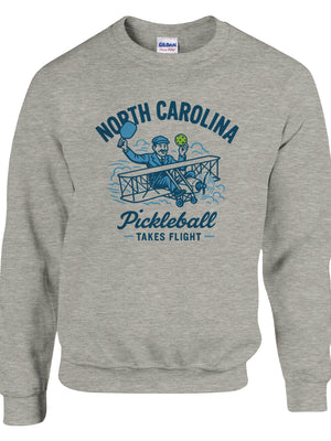 Pickleball sweatshirt featuring Orville Wright's first flight holding a pickleball with the text “North Carolina Pickleball Takes Flight”.