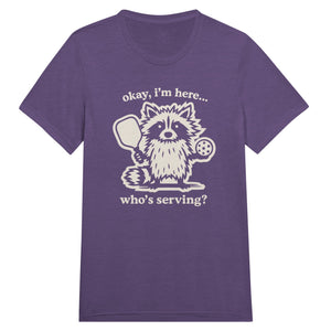 Funny pickleball graphic featuring a raccoon holding a paddle and pickleball with the text “Okay, I’m Here… Who’s Serving?”