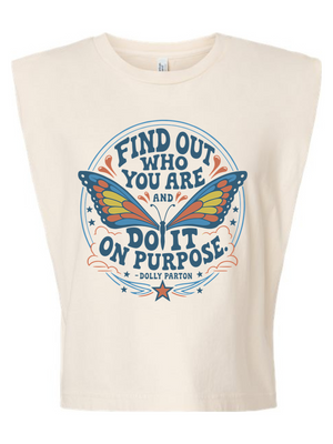 An off-white sleeveless crop top featuring a colorful graphic print of a butterfly inside a circular frame with the text 'FIND OUT WHO YOU ARE AND DO IT ON PURPOSE - DOLLY PARTON'.
