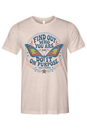 A light beige crewneck t-shirt featuring a colorful retro-style graphic with a butterfly and the quote 'FIND OUT WHO YOU ARE AND DO IT ON PURPOSE' by Dolly Pardon