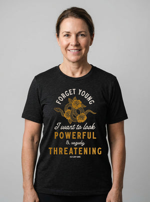 Woman wearing a black heathered t-shirt that reads Forget Young I want to look powerful & vaguely threatening with a snake and roses on it.