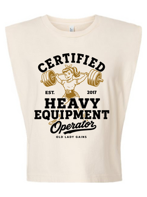 A sleeveless cream-colored crop top featuring a vintage-style graphic that reads 'CERTIFIED HEAVY EQUIPMENT Operator' with an illustration of an older woman lifting a barbell.