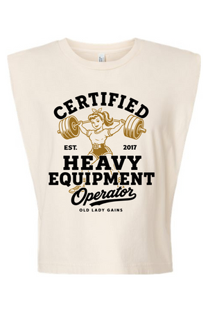 A sleeveless cream-colored crop top featuring a vintage-style graphic that reads 'CERTIFIED HEAVY EQUIPMENT Operator' with an illustration of an older woman lifting a barbell.