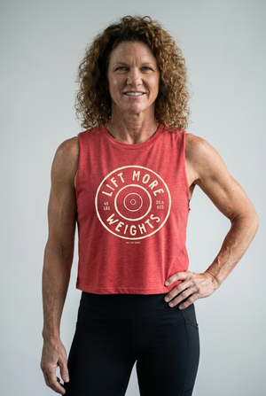 Confident middle-aged woman wearing a red tank top with 'Lift More Weights' text on a white background