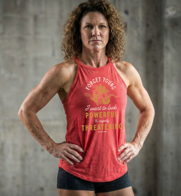 Woman wearing a red workout tank top with empowering text in front of a concrete wall.