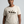 A woman wearing a light beige crewneck t-shirt with a graphic of three figures riding horses and the text 'RAISING UNGOVERNABLE. RAISING UNGOVERNABLE.