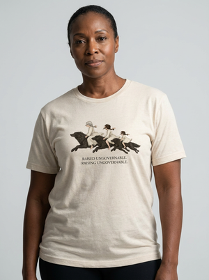 A woman wearing a light beige crewneck t-shirt with a graphic of three figures riding horses and the text 'RAISING UNGOVERNABLE. RAISING UNGOVERNABLE.