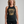 A woman modeling a dark charcoal gray halter tank top with a distressed gold graphic that reads 'THE HELL I CAN'T' with wings and stars, paired with black leggings against a light gray studio background.
