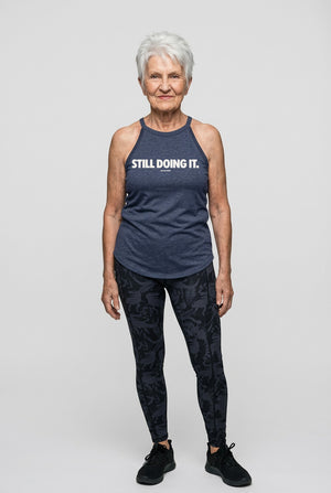 Confident older woman in workout tank top with bold “Still Doing It” graphic fitness clothing