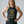 A woman modeling a dark charcoal gray racerback tank top with a gold graphic print that reads 'FORGET YOUNG I want to look POWERFUL & vaguley THREATENING'.