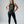 A woman modeling a dark charcoal gray racerback tank top with a gold graphic print that reads 'FORGET YOUNG I want to look POWERFUL & vaguley THREATENING'.