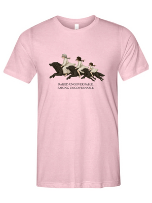 A light pink short-sleeve crewneck t-shirt featuring a graphic of three women riding horses across a field, with the text 'RAISED UNGOVERNABLE. RAISING UNGOVERNABLE.