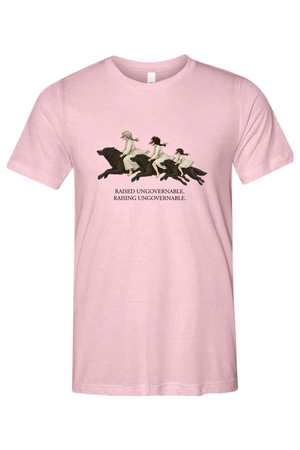A light pink short-sleeve crewneck t-shirt featuring a graphic of three women riding horses across a field, with the text 'RAISED UNGOVERNABLE. RAISING UNGOVERNABLE.