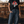 Woman wearing a black t-shirt with a graphic design and text, standing in front of a wooden wall.