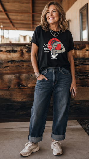 Woman wearing a black t-shirt with a graphic design and text, standing in front of a wooden wall.