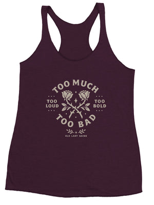 Strong middle-aged woman flexing in a racerback tank that reads Too Loud Too Bold Too Much Too Bad.