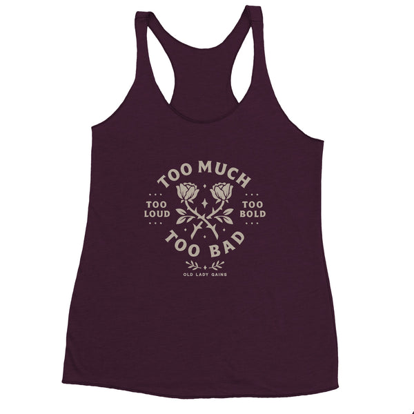 Strong middle-aged woman flexing in a racerback tank that reads Too Loud Too Bold Too Much Too Bad.