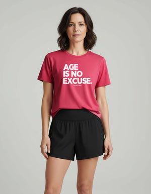 strong Woman over 40 wearing a berry t-shirt with 'AGE IS NO EXCUSE' text on a gray background