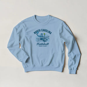 Pickleball sweatshirt featuring Orville Wright's first flight holding a pickleball with the text “North Carolina Pickleball Takes Flight”.