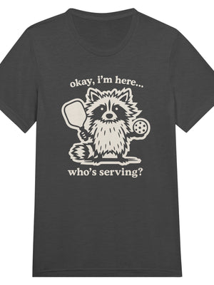Funny pickleball graphic featuring a raccoon holding a paddle and pickleball with the text “Okay, I’m Here… Who’s Serving?”
