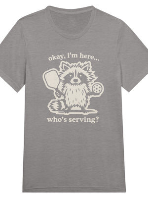 Funny pickleball graphic featuring a raccoon holding a paddle and pickleball with the text “Okay, I’m Here… Who’s Serving?”