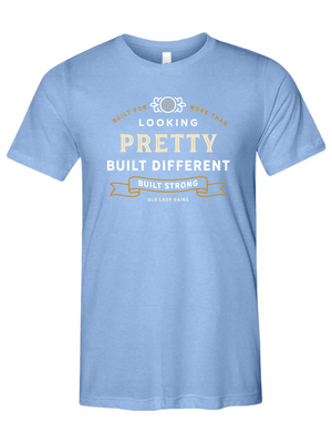 Woman's light blue t-shirt reading "Built for More Than Looking Pretty. Built Different. Built Strong." by Old Lady Gains, motivational fitness apparel for women over 40.