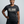 A smiling woman wearing a dark heather gray t-shirt with 'FULL MOON ENERGY' printed in beige on the chest, paired with black athletic leggings, against a light gray studio background.