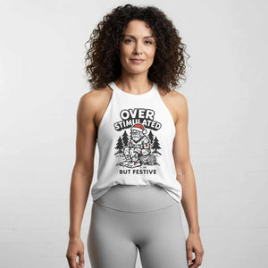 Vintage-style illustration of a tired female Sasquatch wearing a Santa hat, tangled in colorful Christmas lights, sitting in the woods under the text ‘Overstimulated But Festive’ on a women’s halter tank by Old Lady Gains.