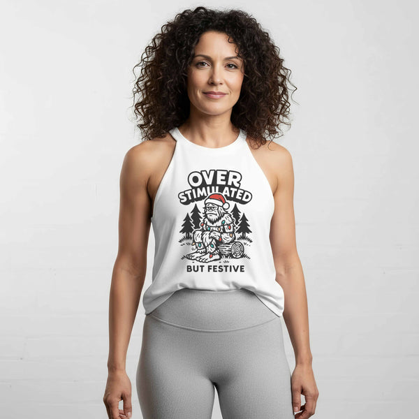 Vintage-style illustration of a tired female Sasquatch wearing a Santa hat, tangled in colorful Christmas lights, sitting in the woods under the text ‘Overstimulated But Festive’ on a women’s halter tank by Old Lady Gains.