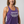 A smiling woman with shoulder-length brown hair wearing a purple heathered racerback tank top with the text 'Someone's Badass Grandma' in white and gray, photographed against a light gray studio background.
